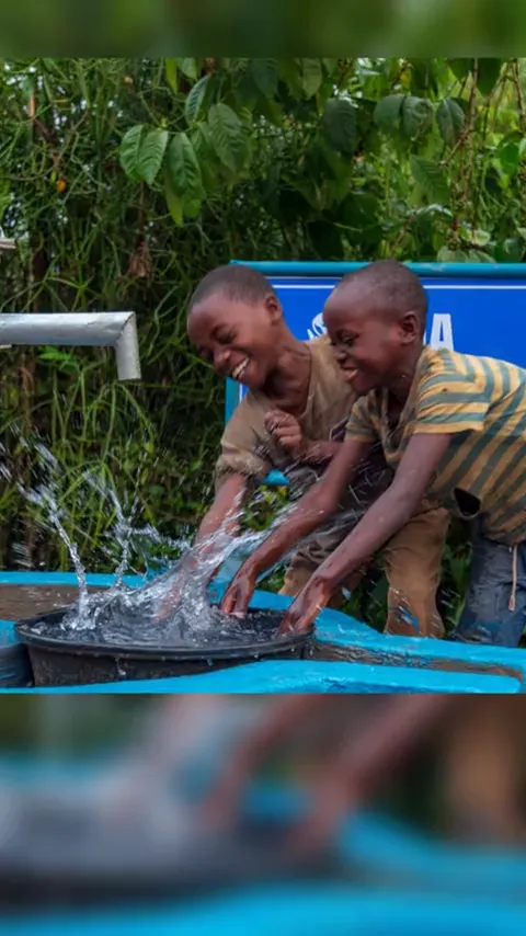 Two boys splashing water at the Mika hand pump